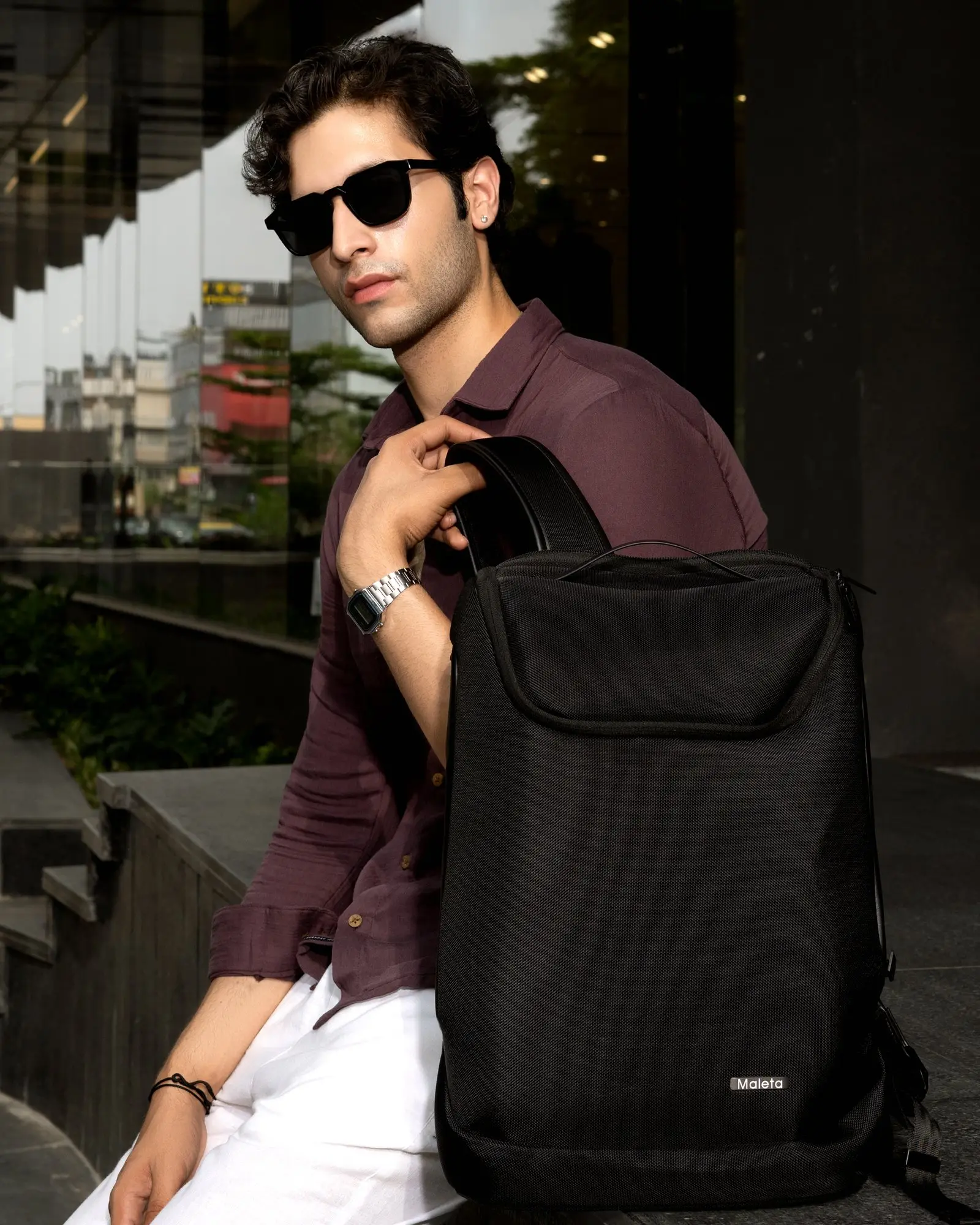 A black laptop backpack worn through the city - glass towers, a terrace, a desk.