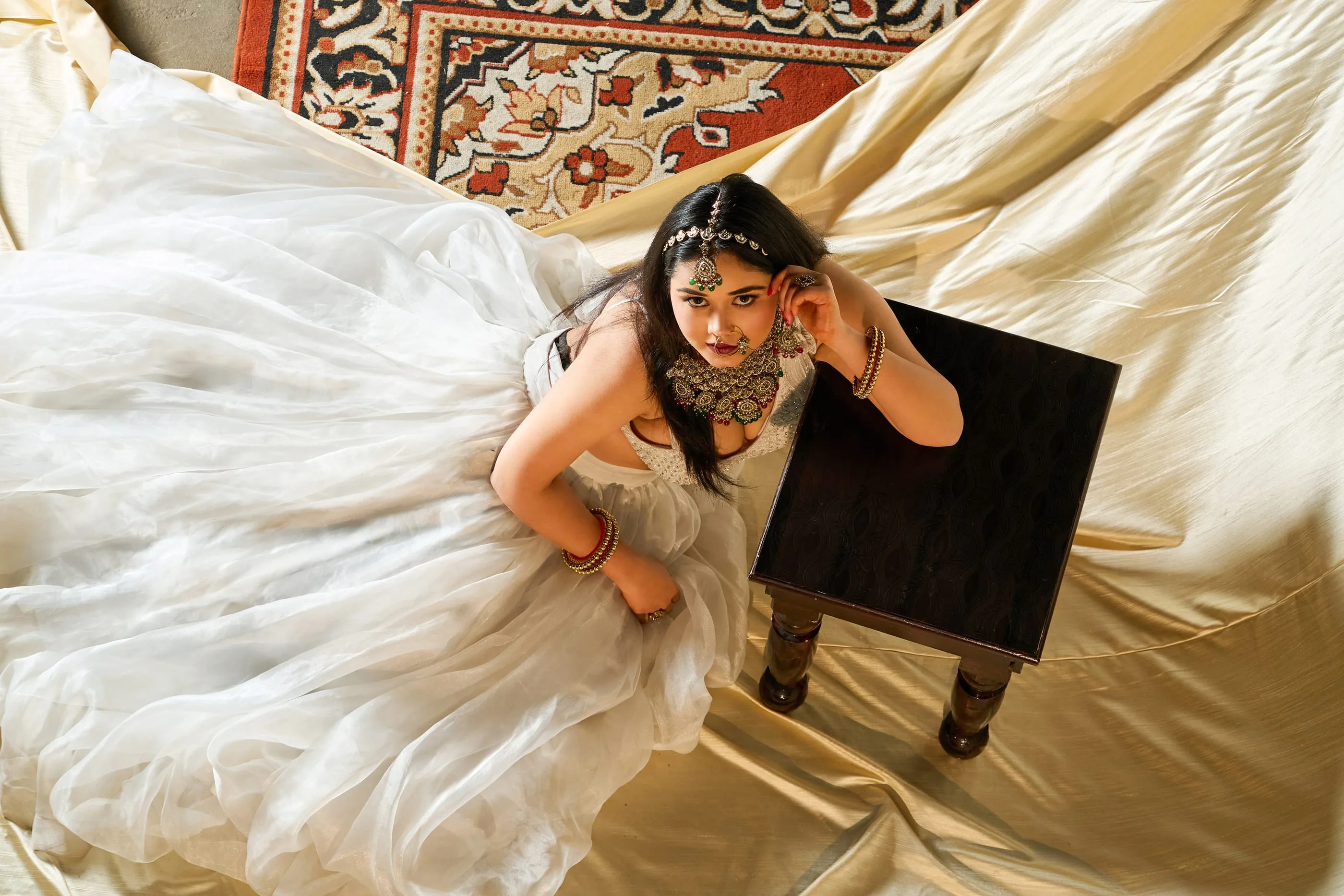 Overhead view of a bride in a white lehenga spread across cream fabric - Raksha Pareek